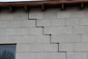 Une fissure en forme d'escalier traversant un mur extérieur construit en blocs de béton gris.
