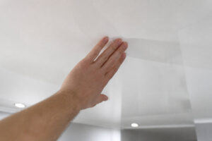 Une main touche délicatement un plafond tendu blanc immaculé pour vérifier la propreté de la surface.