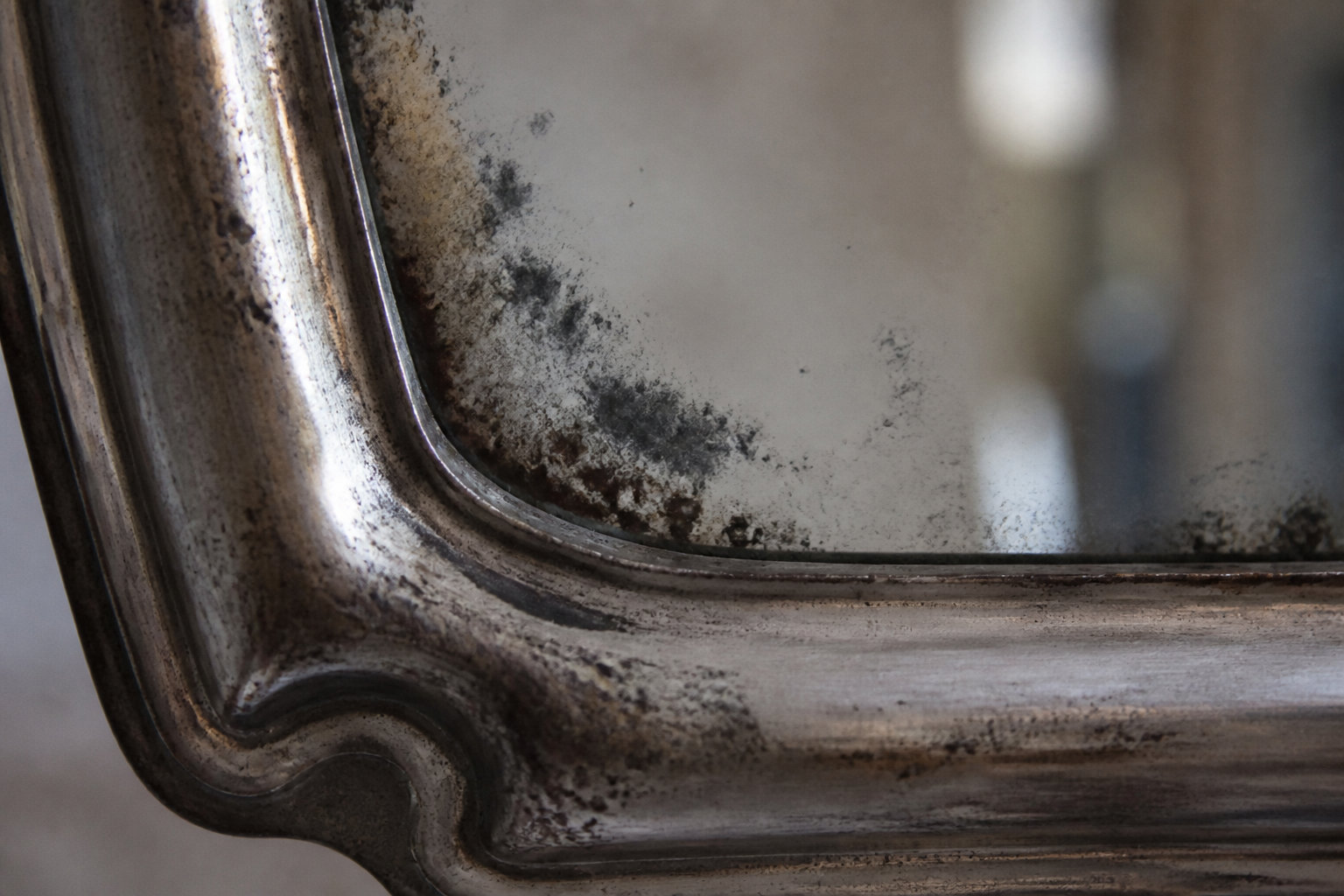 Gros plan sur l'angle d'un miroir ancien montrant des taches d'oxydation sombre causées par l'humidité.