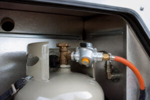 Bouteille de gaz grise avec détendeur raccordée dans le coffre d'un véhicule de loisirs.