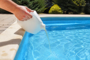 Main versant un produit chimique de traitement dans l'eau d'une piscine bleue.