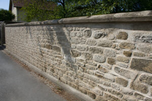 Un mur de clôture traditionnel en moellons de pierre naturelle bordant une route sous un soleil éclatant.