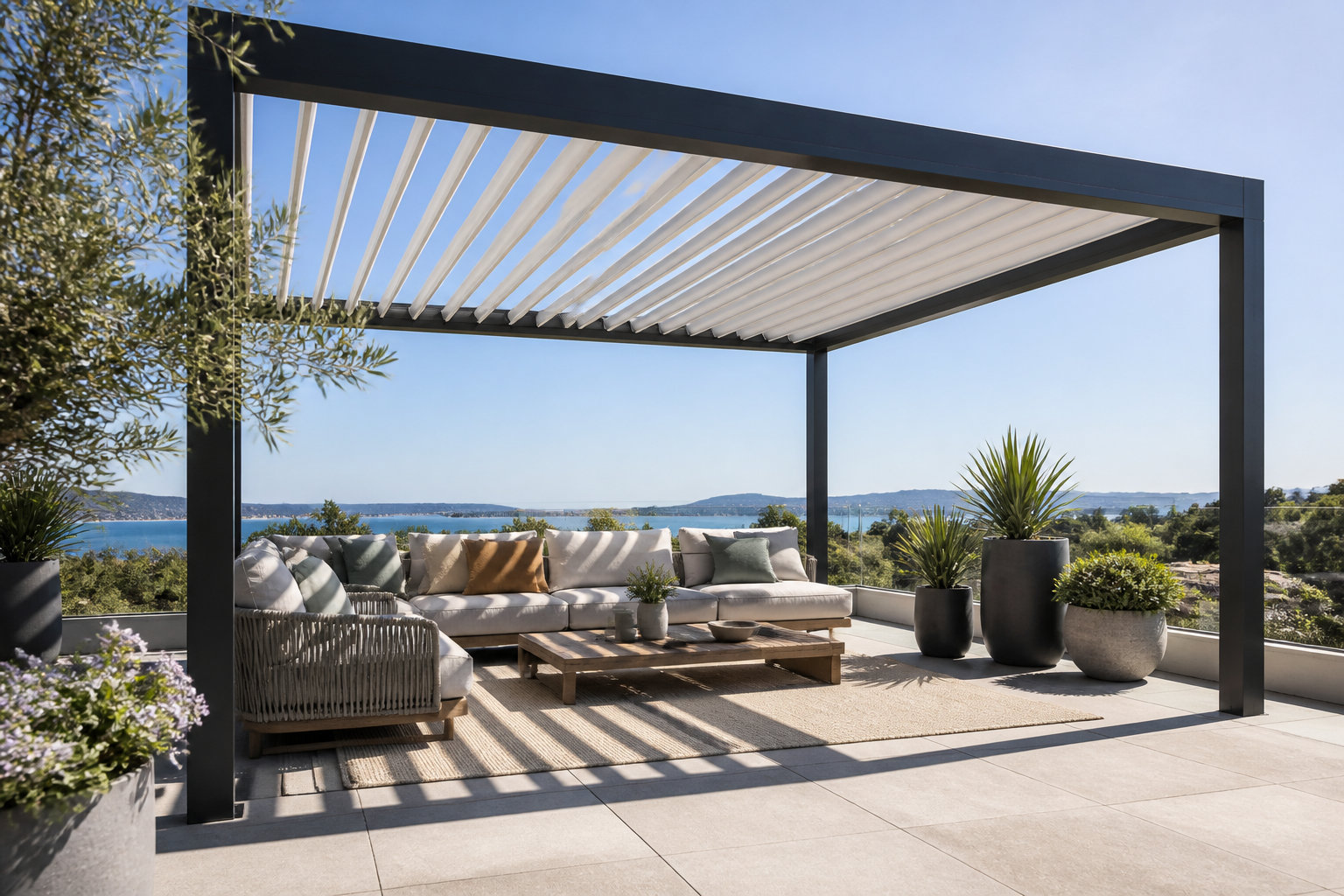Pergola bioclimatique noire sur une terrasse avec salon de jardin et vue panoramique sur la mer sous un ciel bleu.