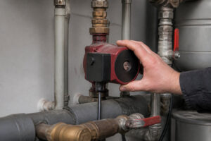 Une main vérifie le circulateur rouge d'une chaudière Domusa sur une installation de chauffage domestique.