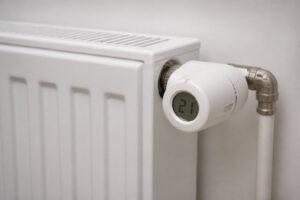 Tête thermostatique numérique réglée sur 21 degrés installée sur un radiateur blanc moderne contre un mur.