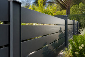 Clôture de jardin moderne composée de lames horizontales en aluminium gris anthracite, entourée de verdure.